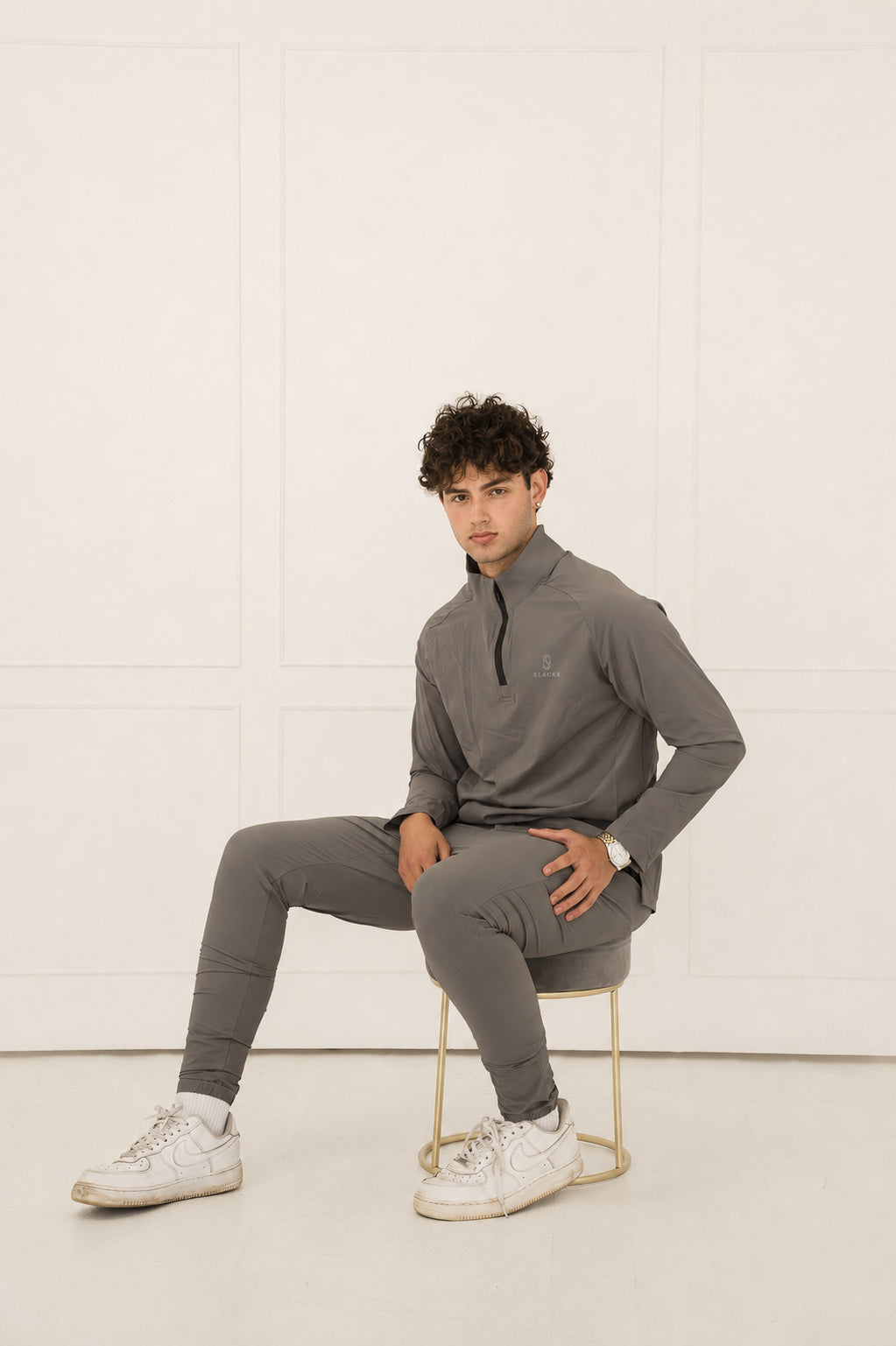 Man wearing the SLACKS grey Baseline Performance Set, seated on a stool